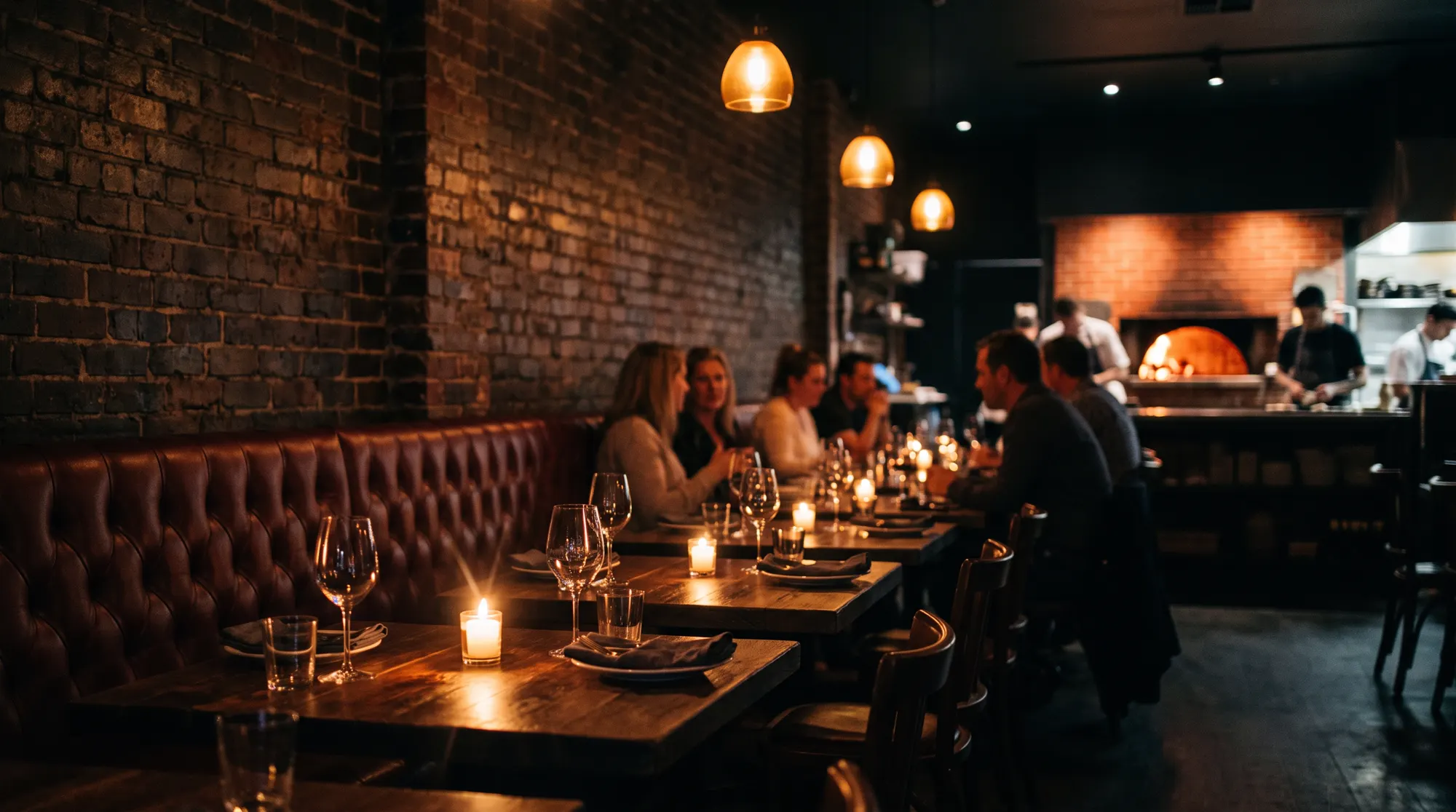 Candlelit dining room with leather banquettes and the oven glowing at the back
